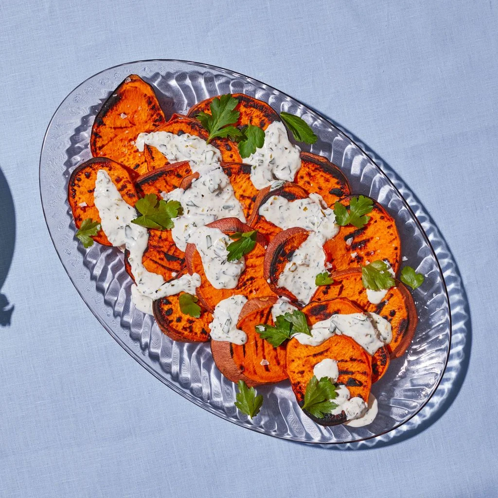 Grilled Sweet Potatoes With Charred Scallion Mayo on a glass plate thats placed on a blue fabric