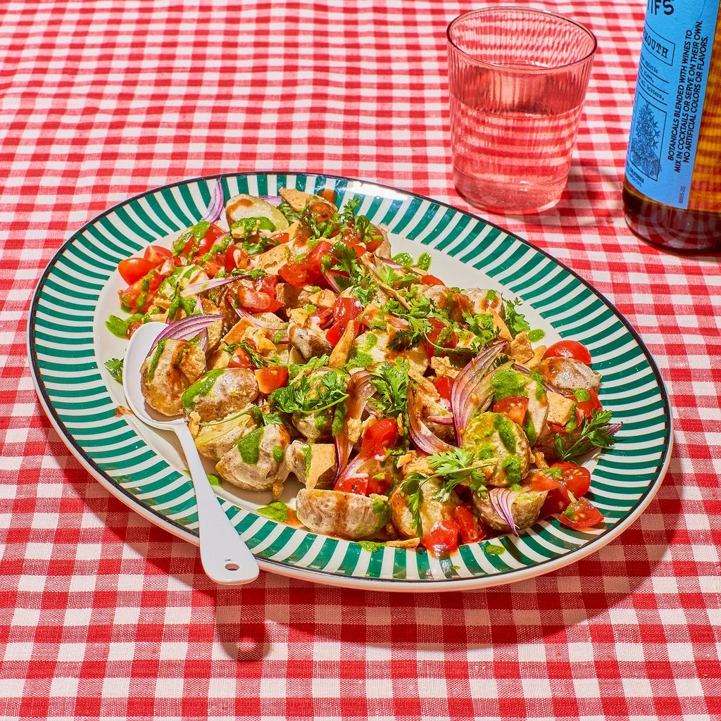 Colorful chaatstyle potato salad with fresh herbs tomatoes and crispy pita chips on a picnic table.