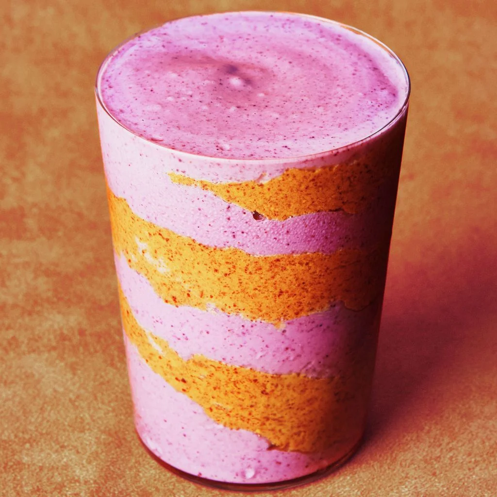 Blended mixed berries cottage cheese water and almond butter in a glass cup with a swirl of almond butter inside.