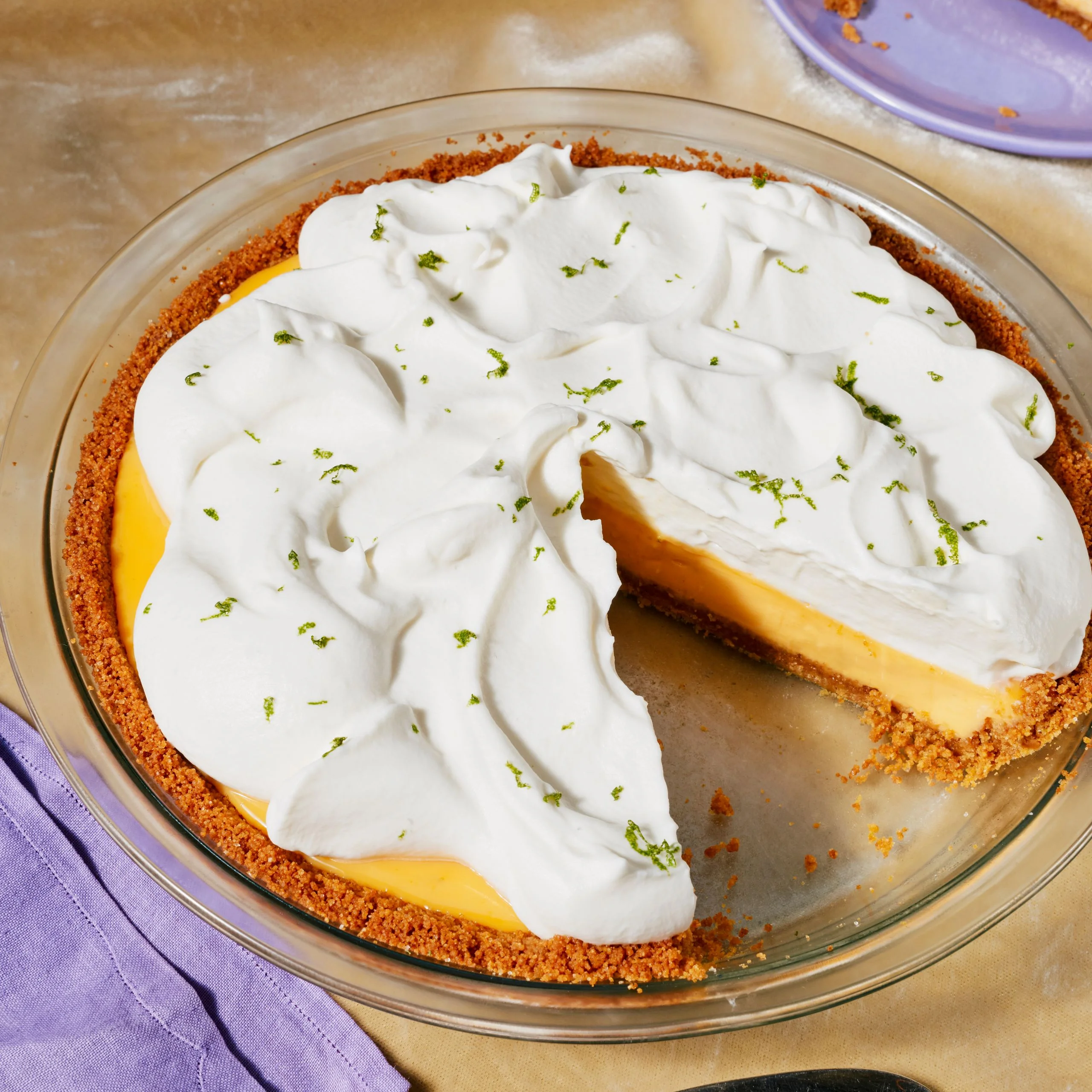 Whole key lime pie topped with whipped cream and lime zest with one slice removed.