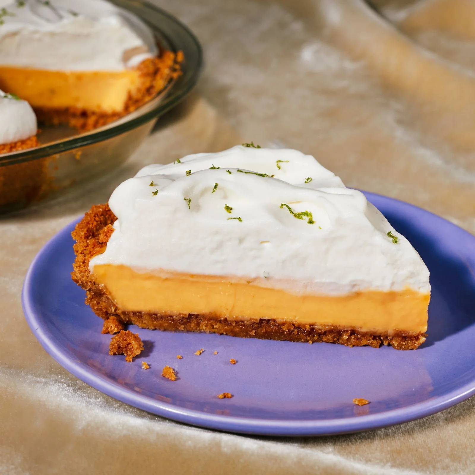 Slice of key lime pie with whipped cream topping and graham cracker crust on a blue plate