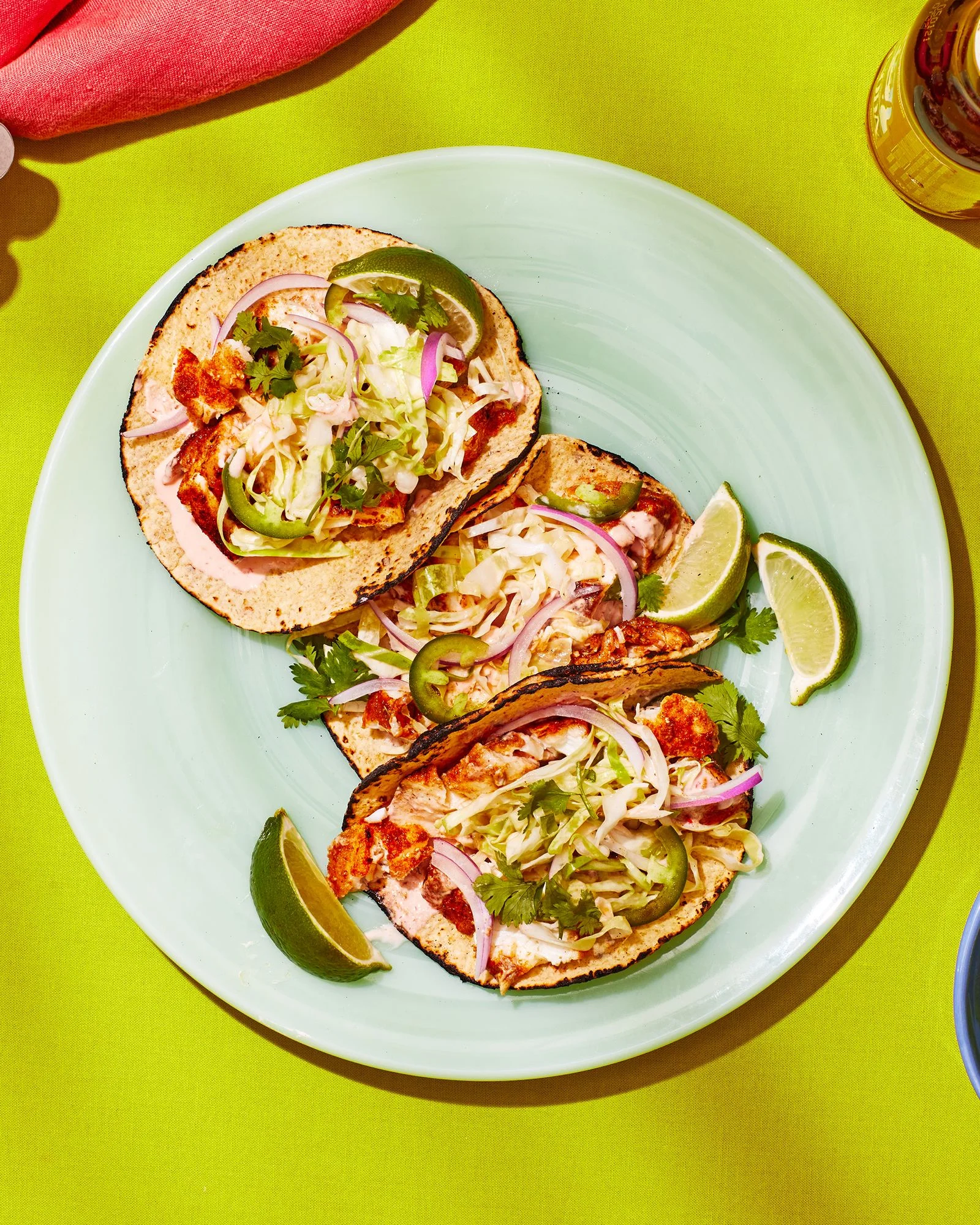 Plate of three fish tacos on a lime green table.
