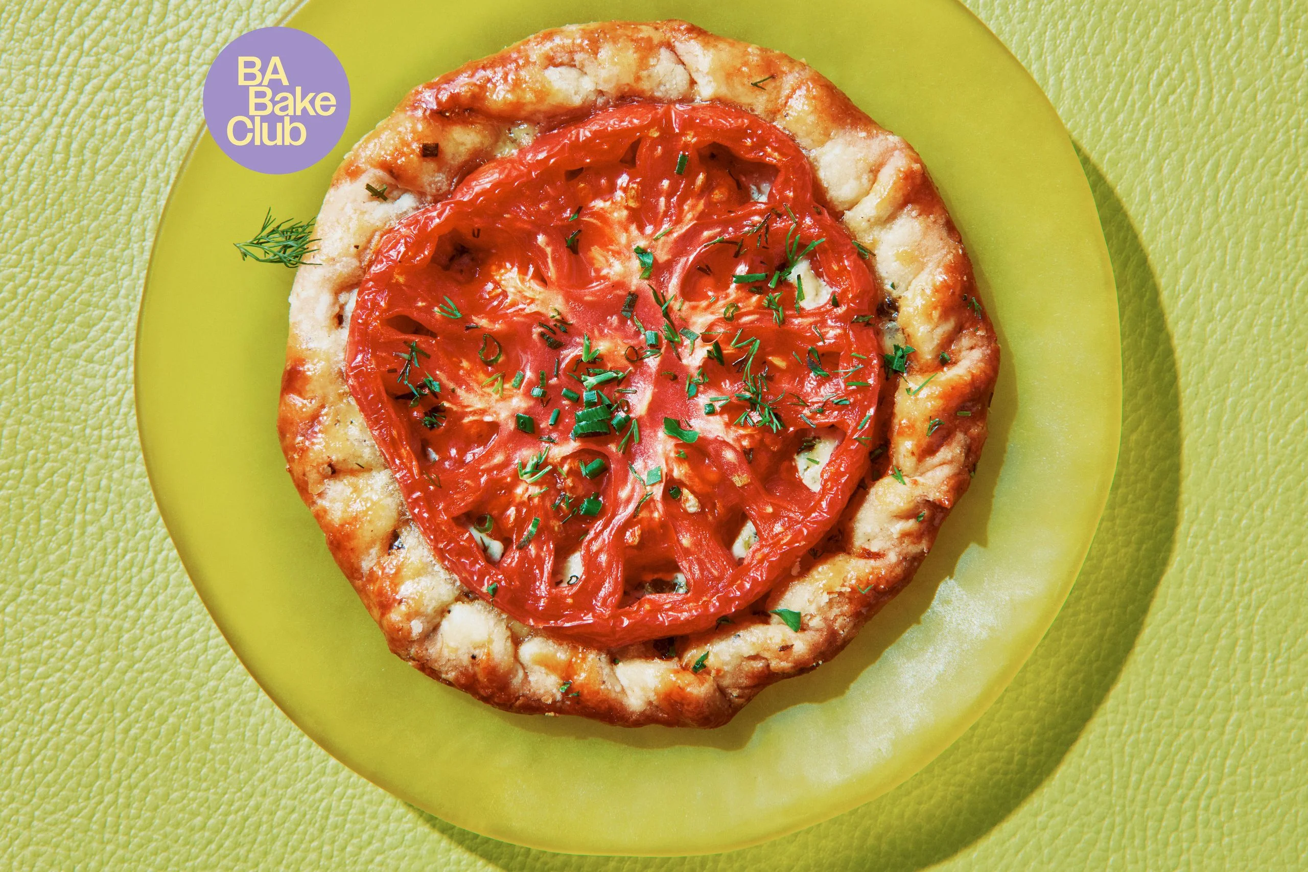 A round of flaky pastry topped with a sliced heirloom tomato chives and dill on a plate.
