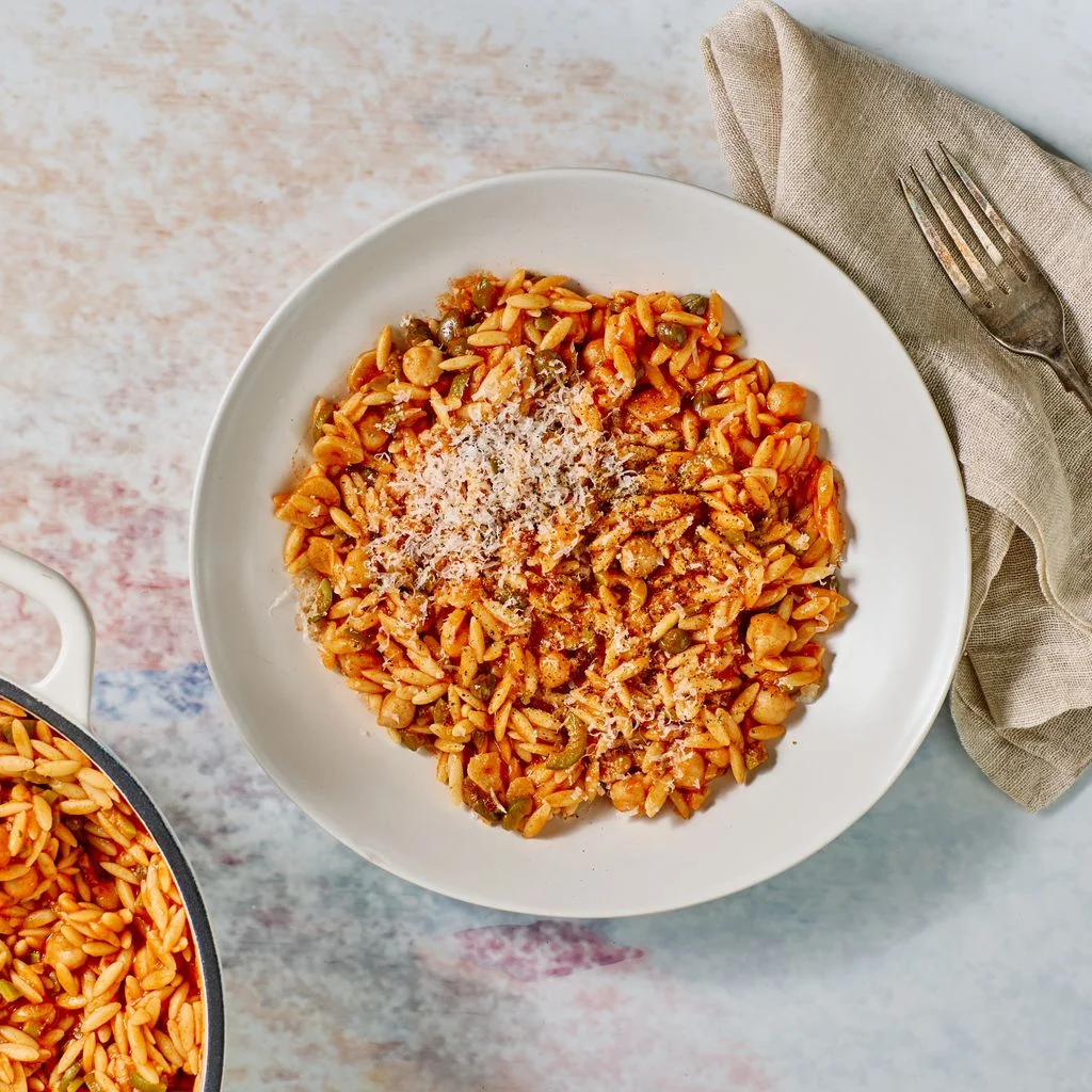 Orzo With Chickpeas in a white bowl placed on top of a multicolored pastel surface