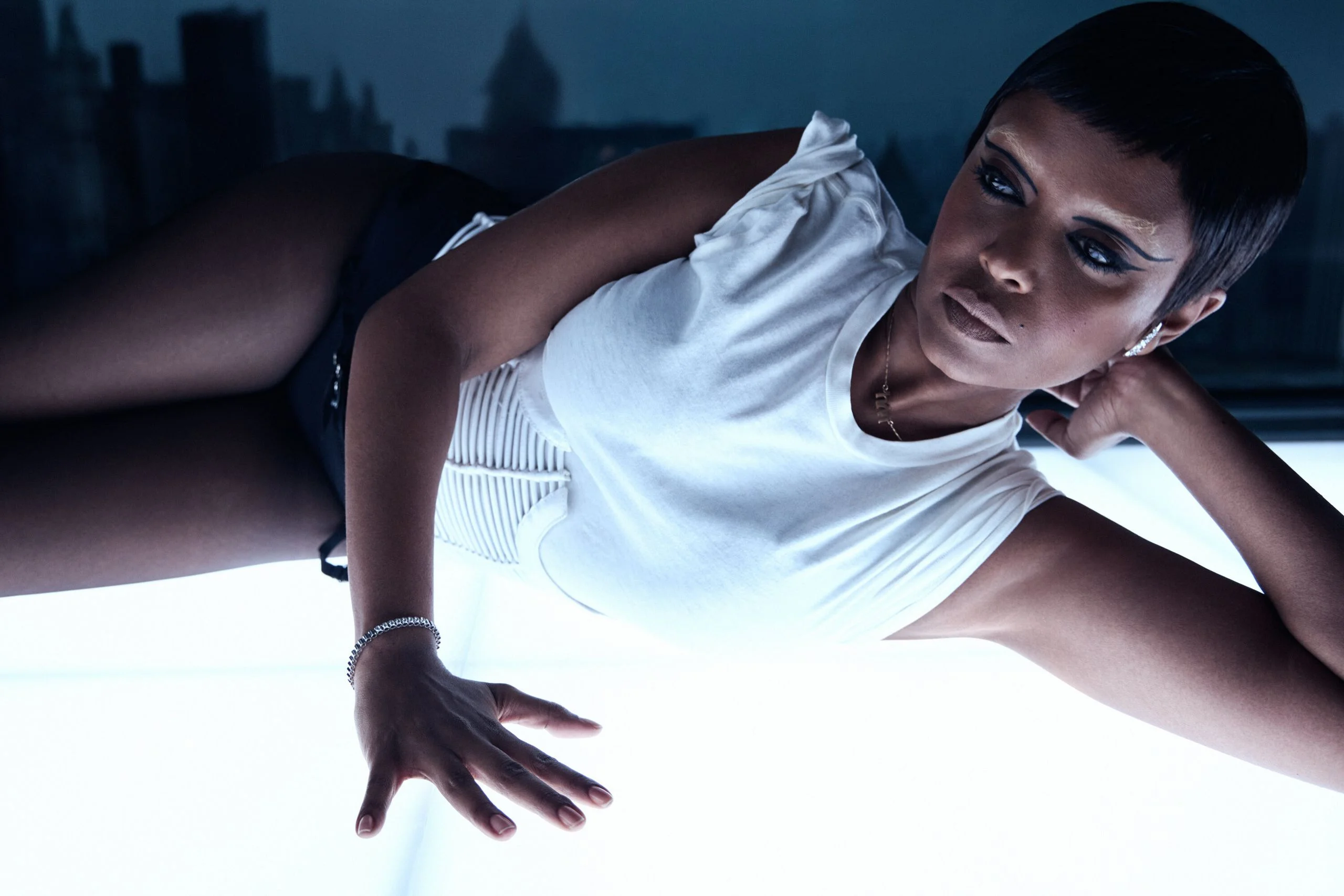 The singer Kelela lying down on a white shining surface