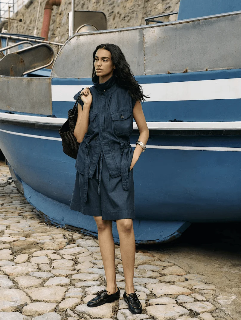 Image may contain Clothing Coat Face Happy Head Person Smile Standing Black Hair Hair Adult Footwear and Shoe