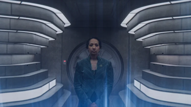 Alexandria Riley as Camille Sims standing in a futuristic room with beams of blue light in the foreground in Silo