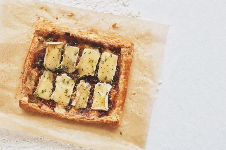 Flaky puff pastry baked with apricot jam slices of brie sprigs of thyme and topped with cracked black pepper.