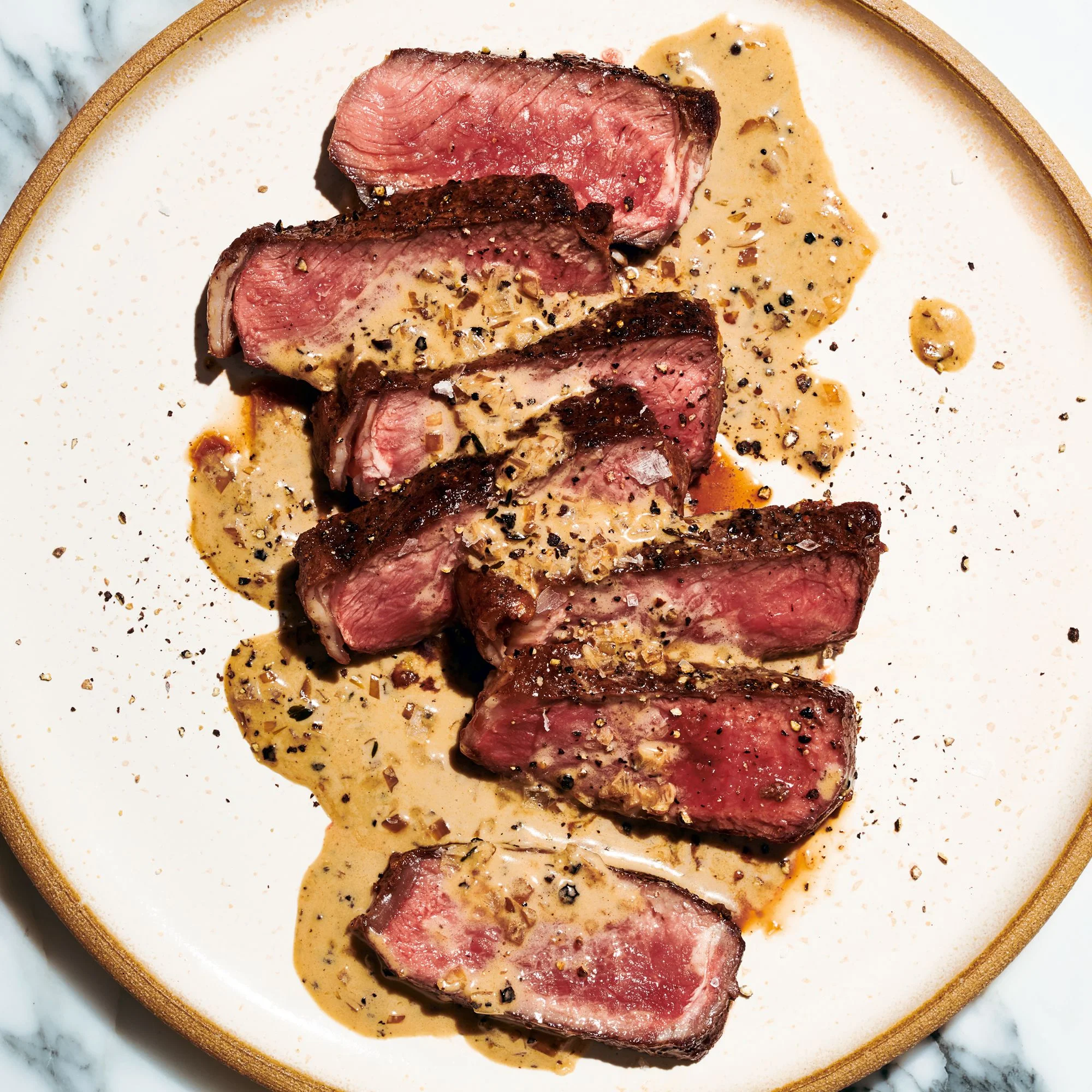 Mediumrare strip steak au poivre sliced and drizzled with creamy black peppercorn sauce