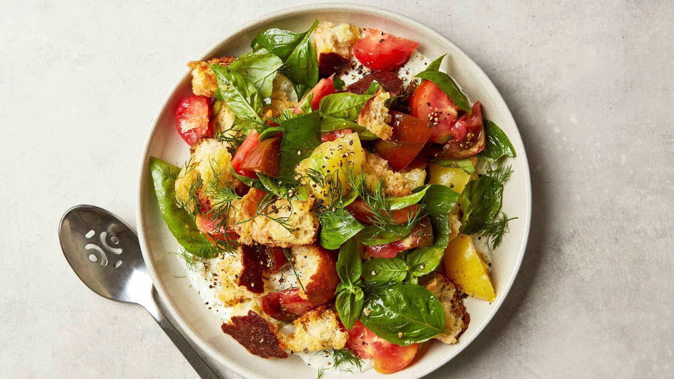 Tomatoes basil dill fronds croutons and pepper on a serving platter.