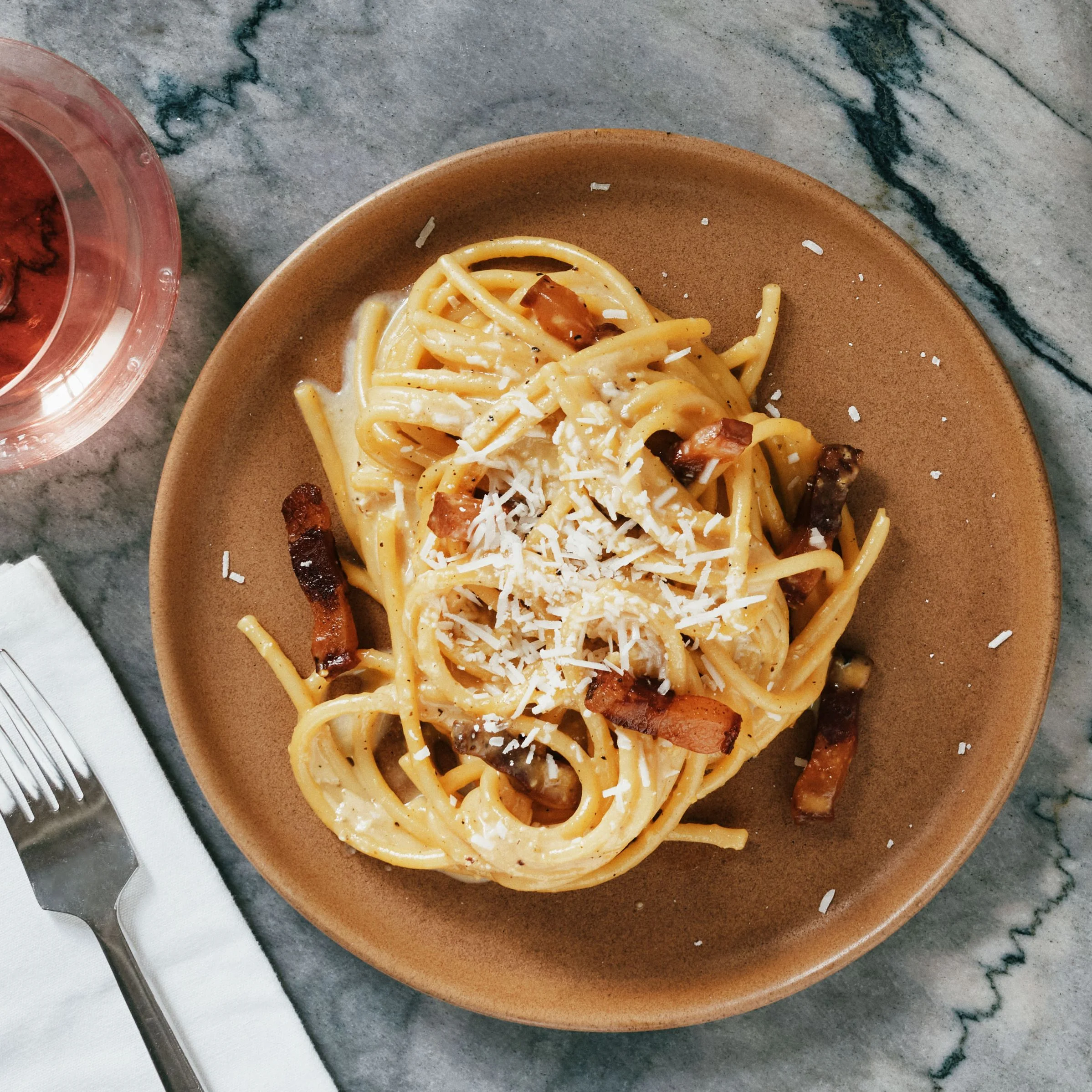 Two plates of spaghetti carbonara with guanciale and shredded Pecorino with glasses of rose.