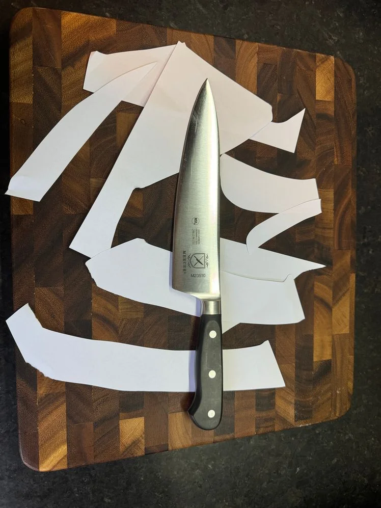 Mercer Renaissance Chef's knife sitting on a cutting board atop sliced pieces of paper