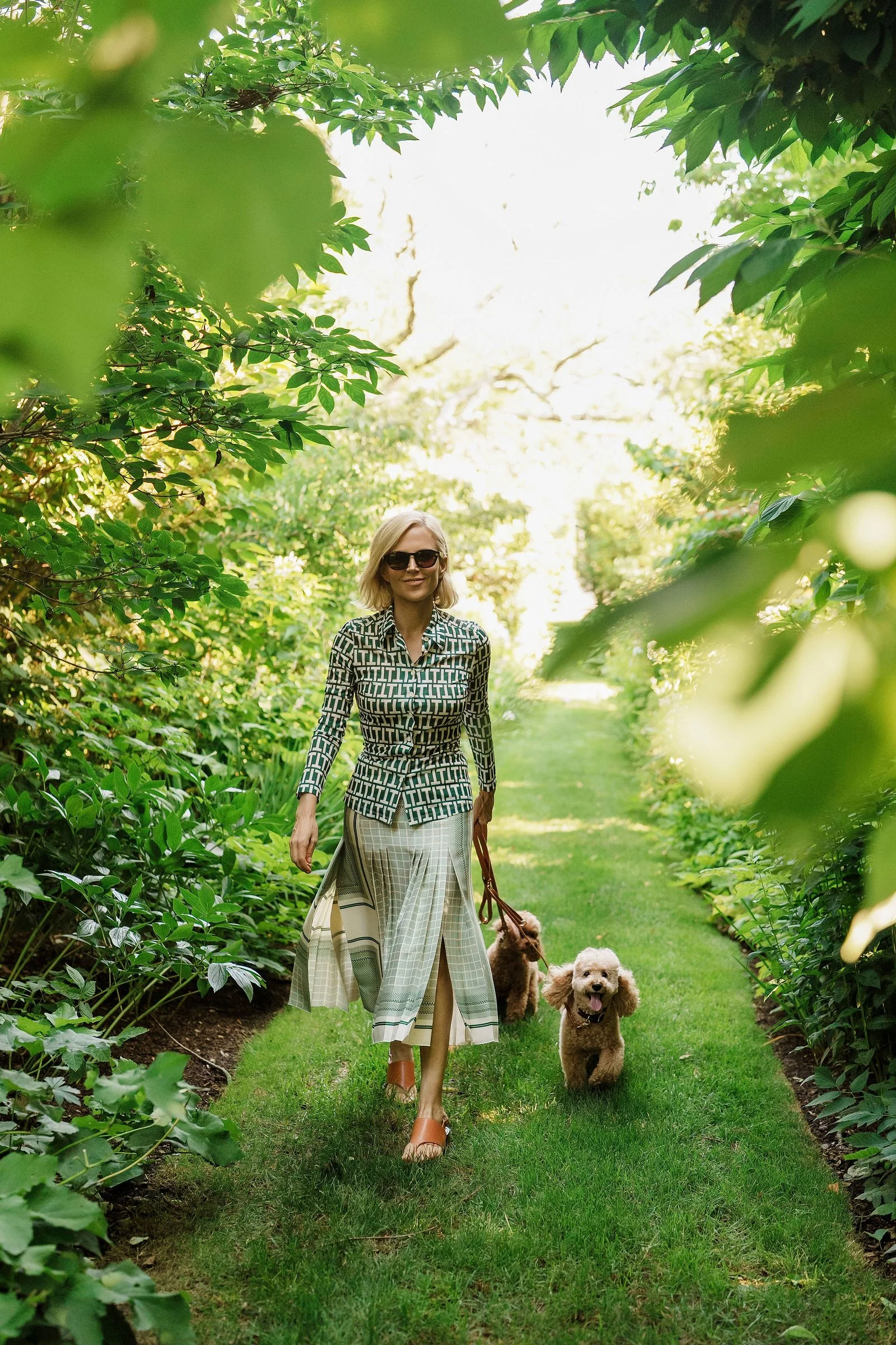 Image may contain Tory Burch Adult Person Animal Canine Mammal Dog Pet Walking Dog Plant and Vegetation