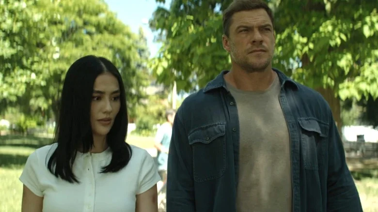 Agnez Mo's Lila Hoth walks alongside Alan Ritchson's Jack Reacher in a park in Reacher