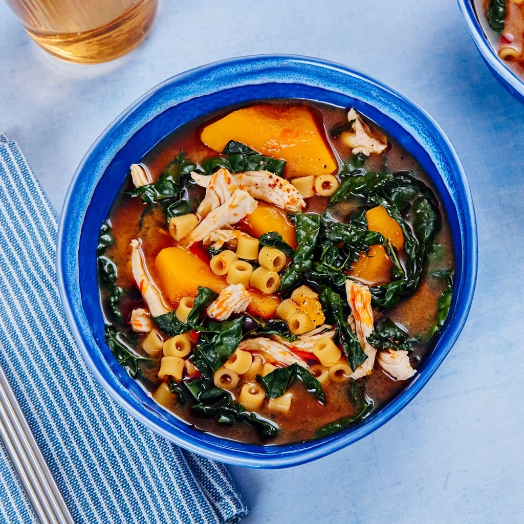 Two bowls of red miso soup with shredded chicken kabocha kale and ditalini.