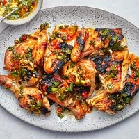 A whole grilled chicken, cut into parts and topped with a scallion-chile relish, on a platter.