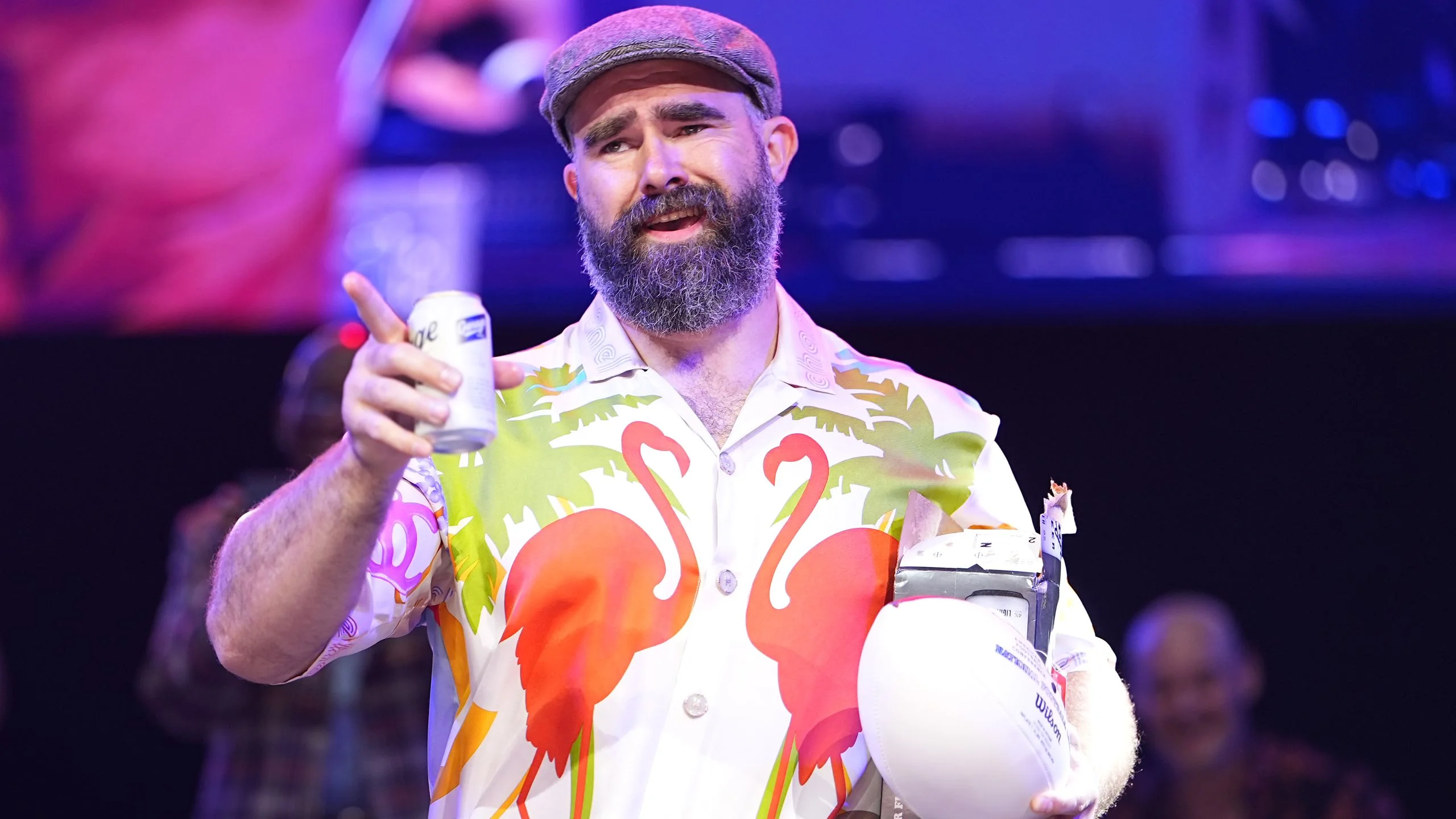 Jason Kelce reacts onstage while holding a Garage beer in onhand and a football in the other