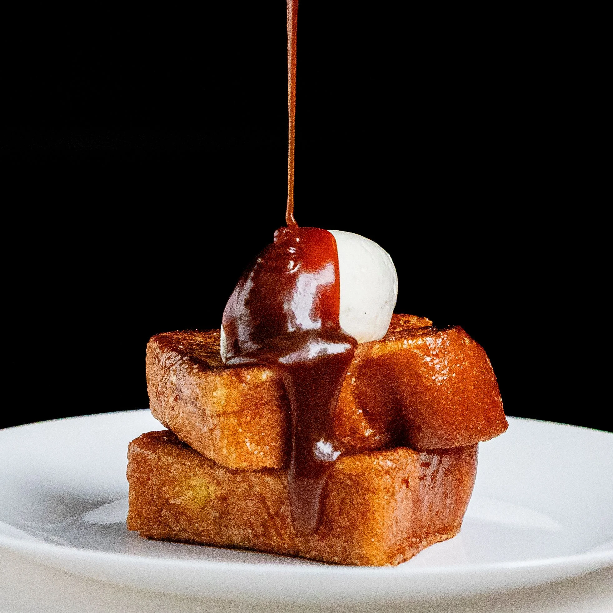 Caramel sauce pouring over two slices of butterfried brioche and a dollop of whipped cream and salt.