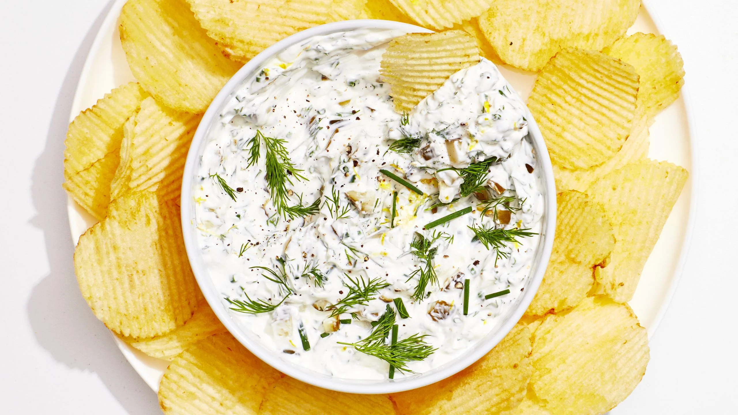 Overhead view of dill pickle dip surrounded by ridged potato chips.