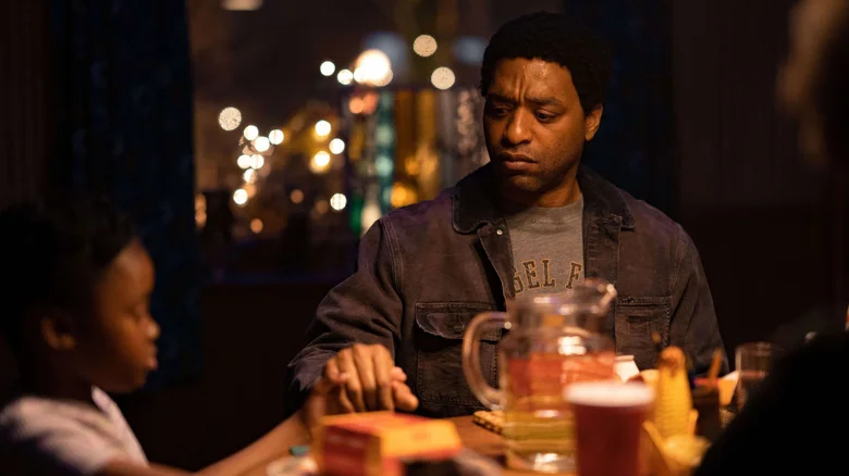 Faraday holding a small child's hand at a dinnertable in The Man Who Fell to Earth