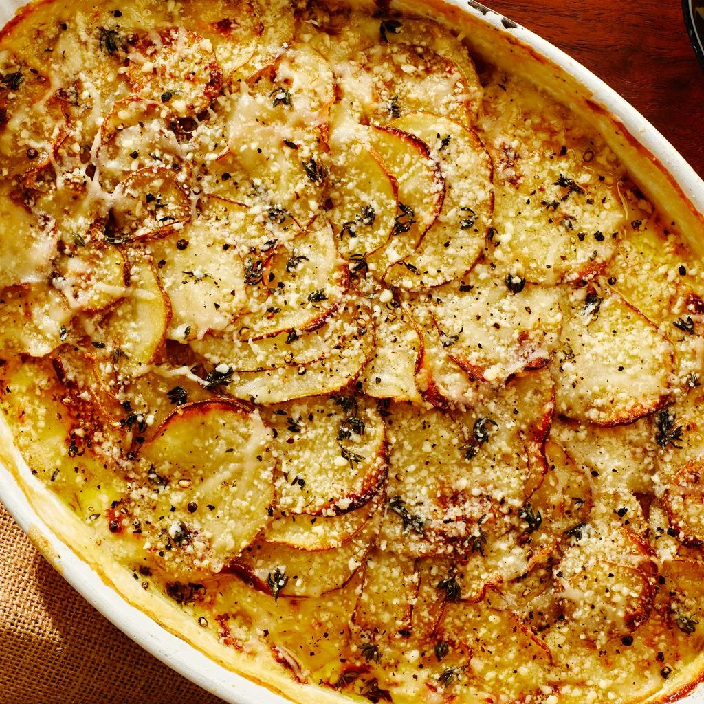 Gratin of potatoes shingled and topped with melted Gruyere and Parmesan in a casserole dish on a wooden surface.