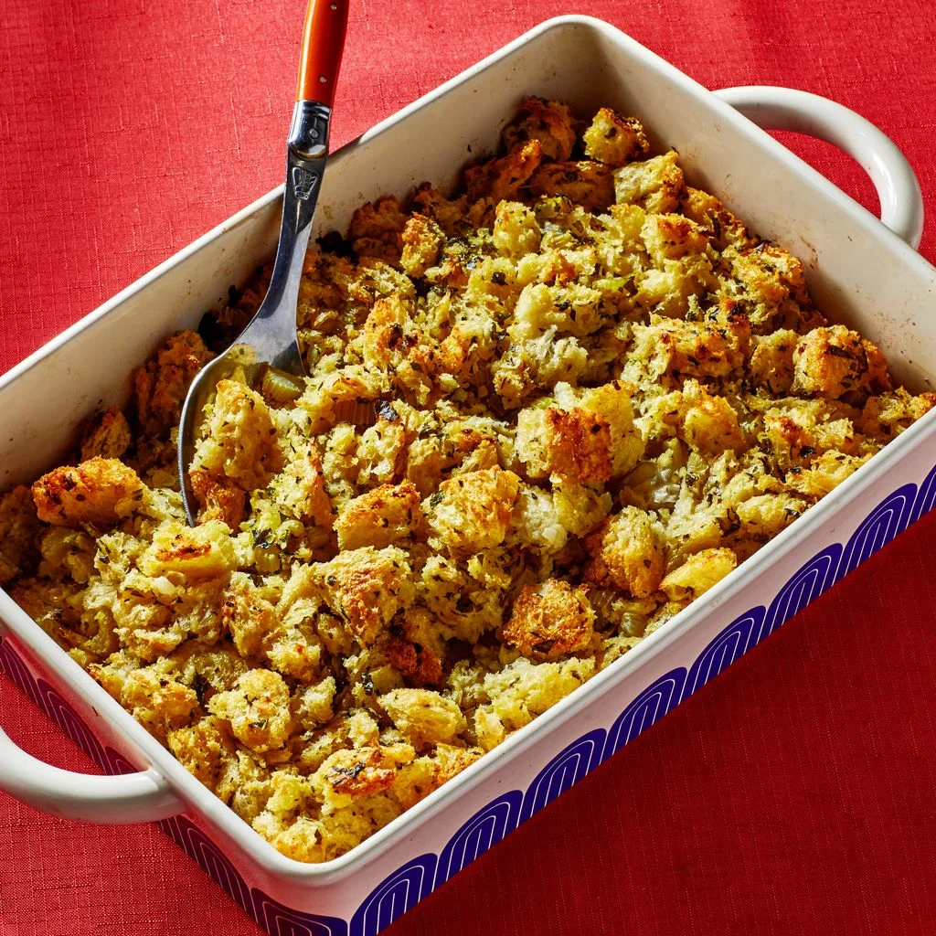 A 13x9 Great Jones ceramic casserole dish filled with a craggy Thanksgiving stuffing set on a red tablecloth.