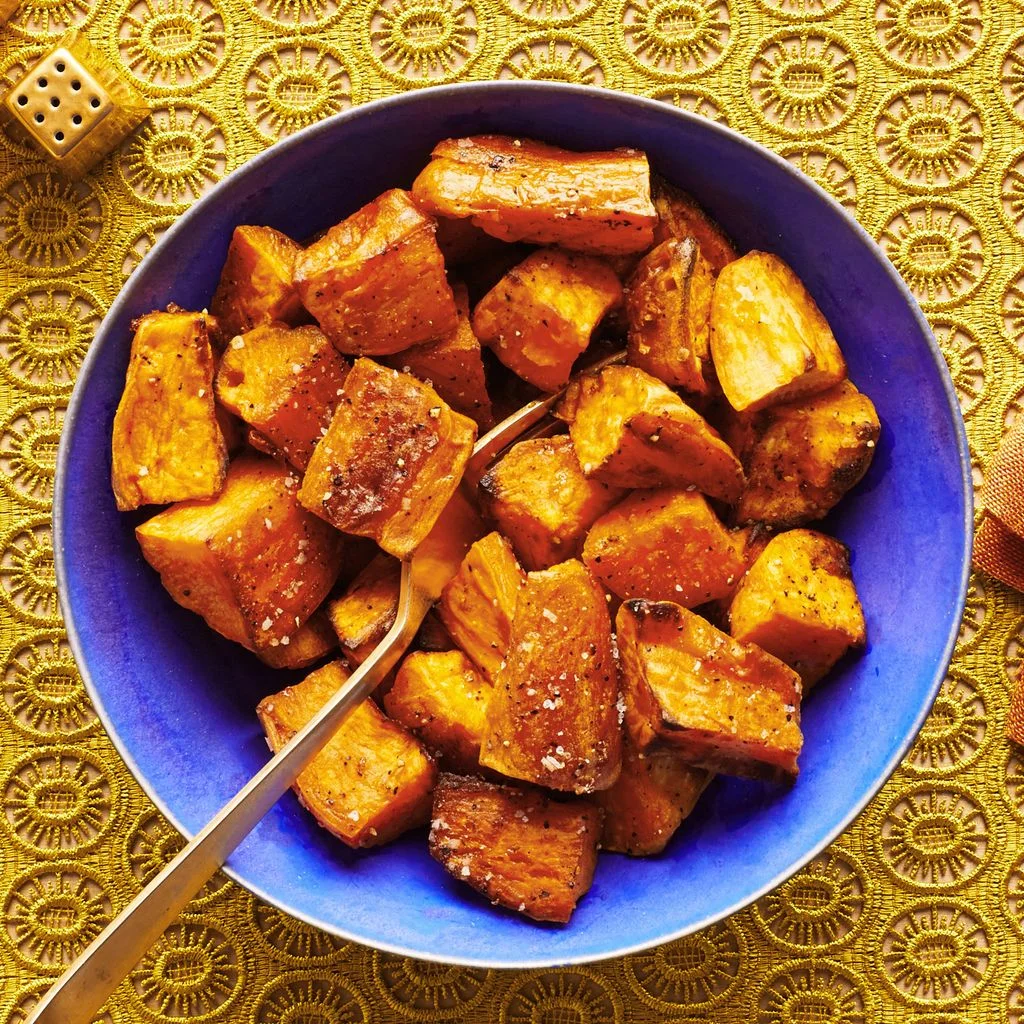 Roasted sweet potatoes in a blue bowl on a yellow tablecloth.