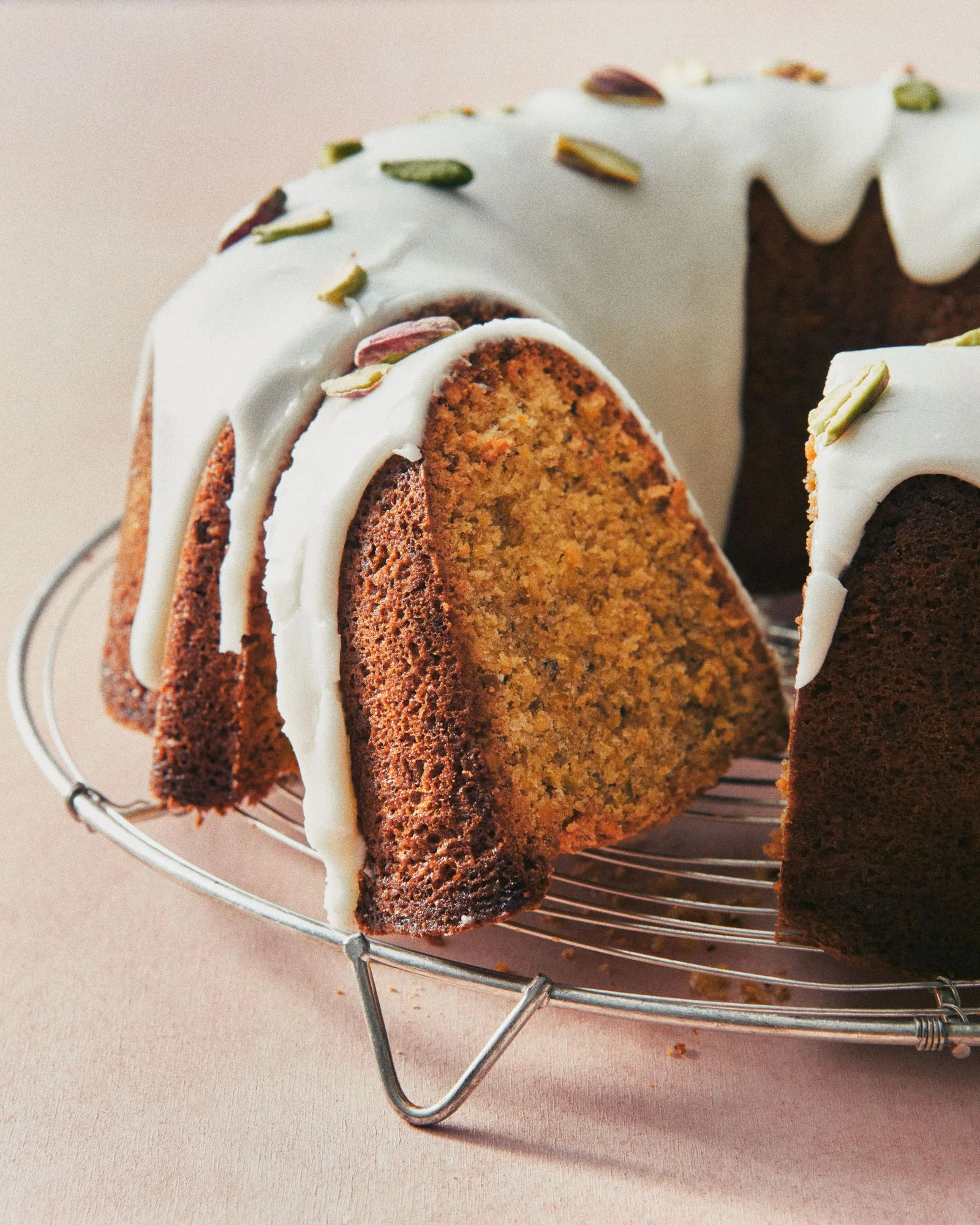A sliced bundt cake on a cooling rack covered in a lemoncream cheese glaze and topped with chopped pistacchi.