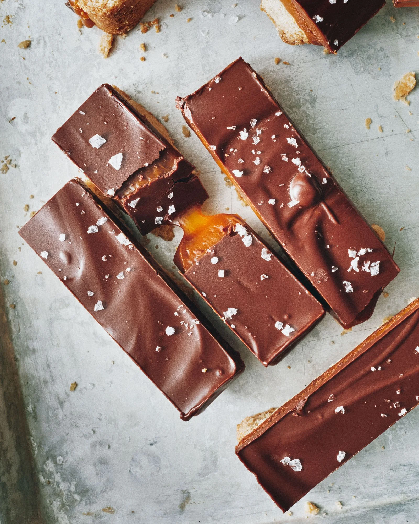 Bars of chocolate caramel and shortbread on a baking sheet topped with flakey salt.