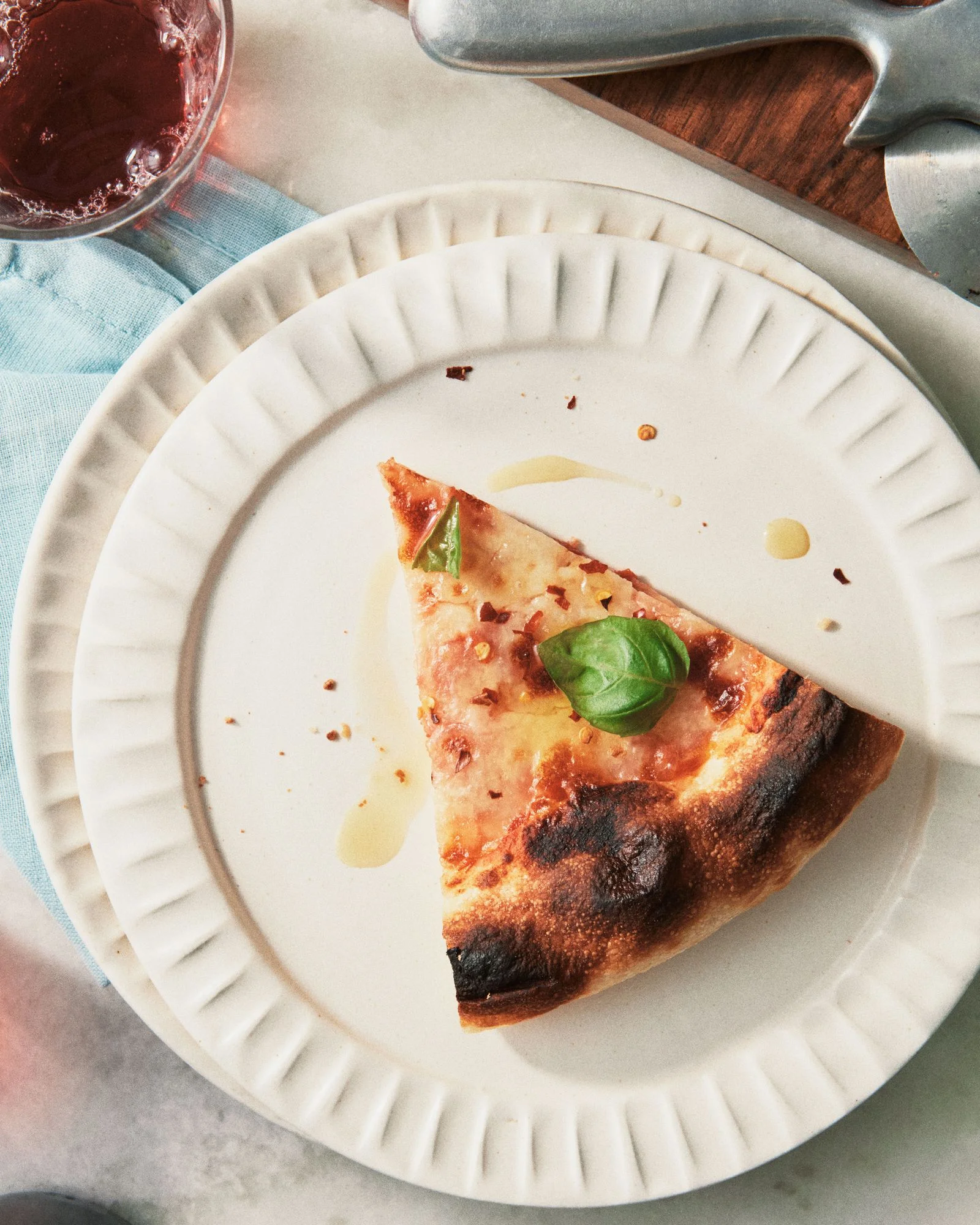 A slice of cheese pizza on a plate topped with red pepper flakes olive oil and basil leaves.