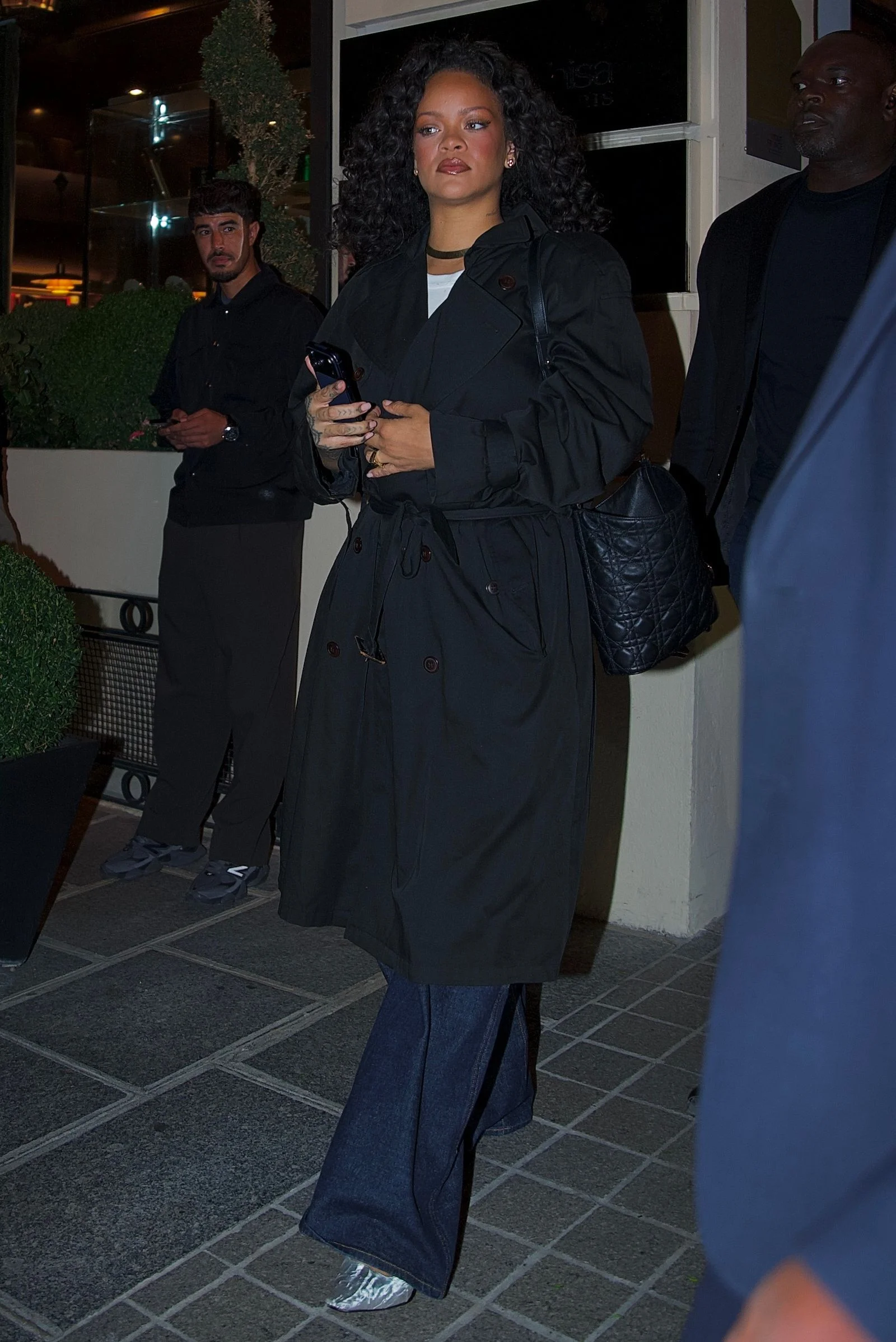 Image may contain Rihanna Clothing Coat Accessories Bag Handbag Overcoat Footwear Shoe Adult Person and Plant
