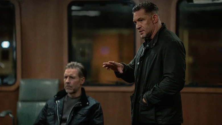 Paddy Considine's Kevin Harrigan sits in a meeting room as Tom Hardy's Harry Da Souza stands next to him in MobLand