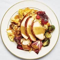 A full Thanksgiving plate with sliced turkey breast topped with gravy, roasted brussels sprouts, stuffing, radicchio salad, and cranberry sauce.