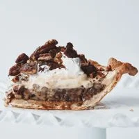 A pie with layers of syrupy chopped pecans, brown sugar custard, whipped cream topped with candied pecans in an Actually Perfect Pie Crust.