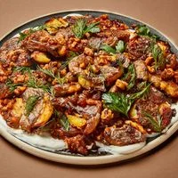 Smashed potatoes, piled on a platter, with yogurt sauce on the bottom and a walnut-and-herb dressing spooned over the top.