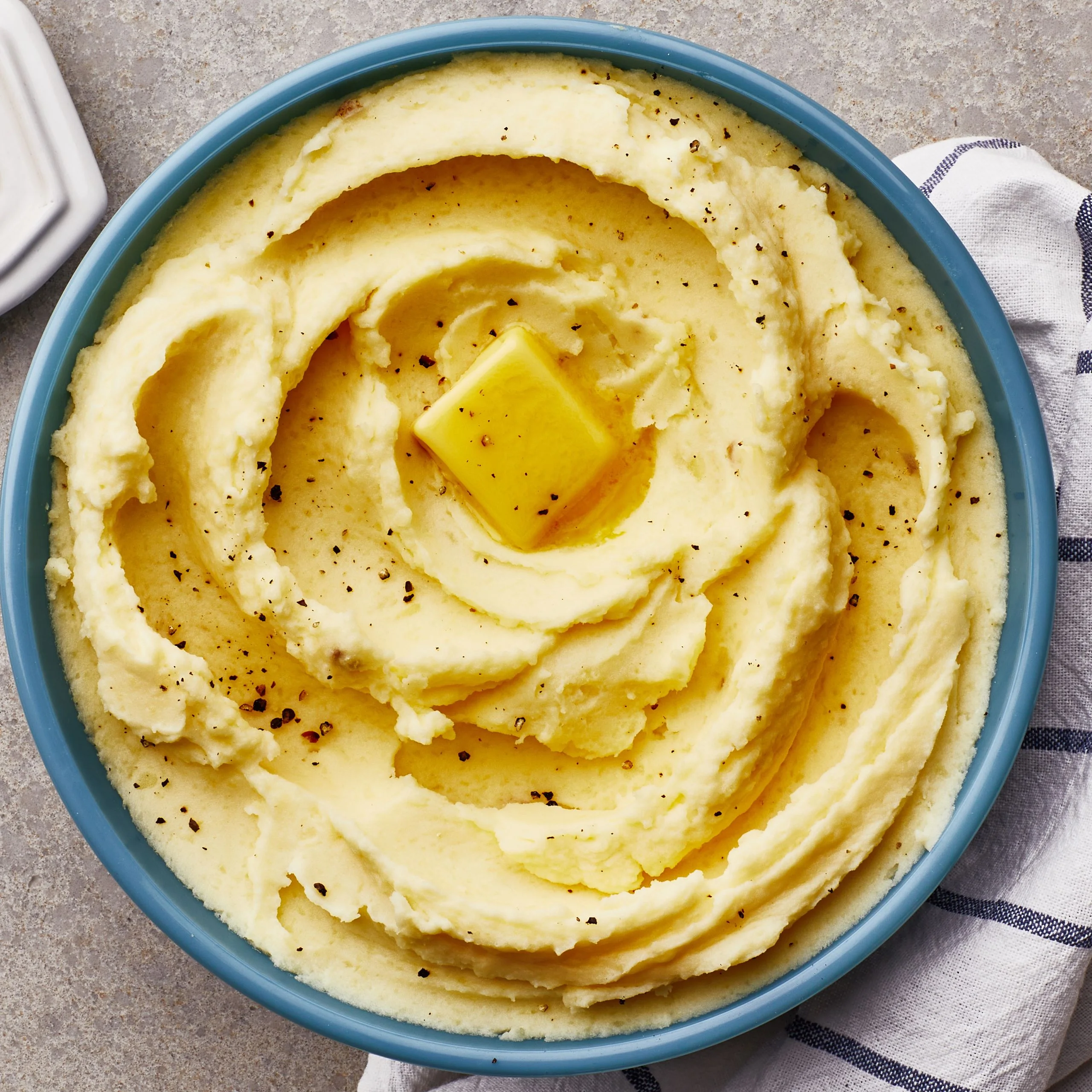 Creamy mashed potatoes topped with butter and black pepper in a blue bowl.