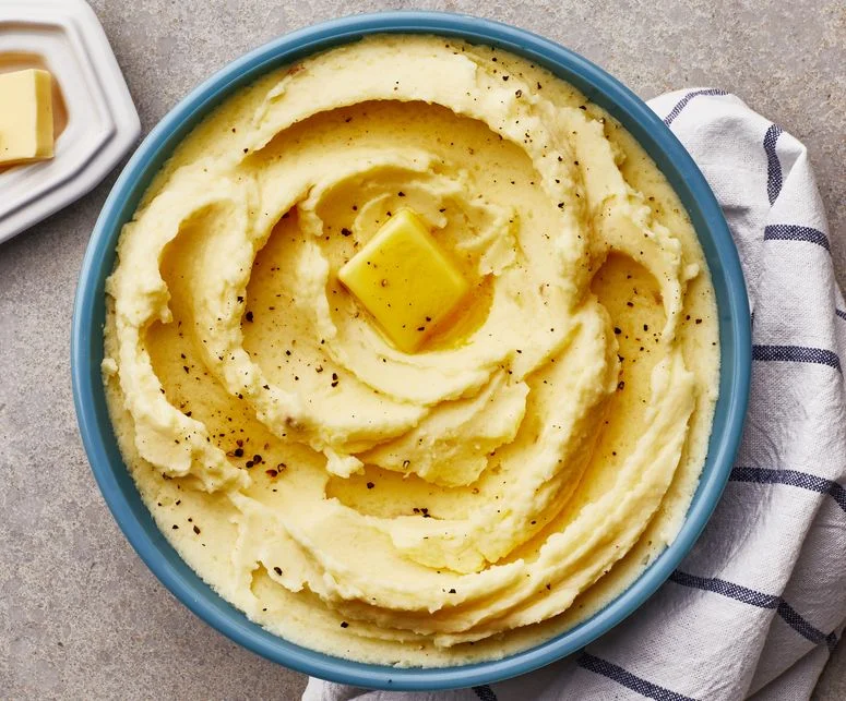 Creamy mashed potatoes topped with butter and black pepper in a blue bowl.