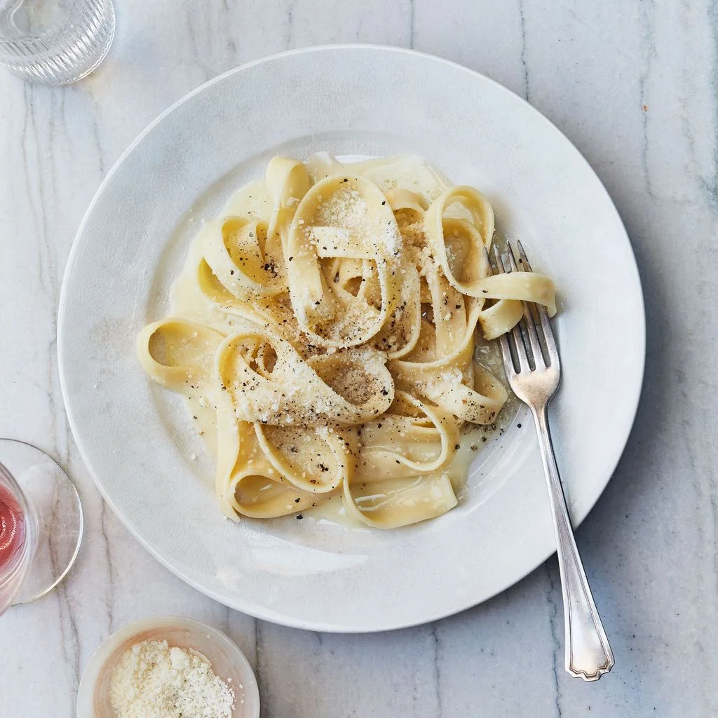A plate of fettuccine Alfredo pasta topped with grated Parmesan and freshly ground black pepper.