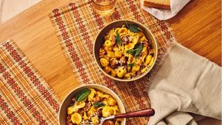 Bowls of pasta with golden beets sausage and fried sage on a plaid tablecloth