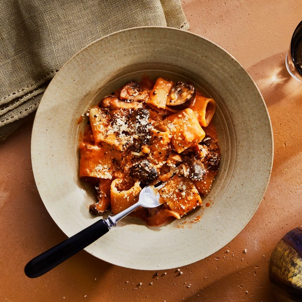 mushroom pasta on a tan background with napkin and drink on the side