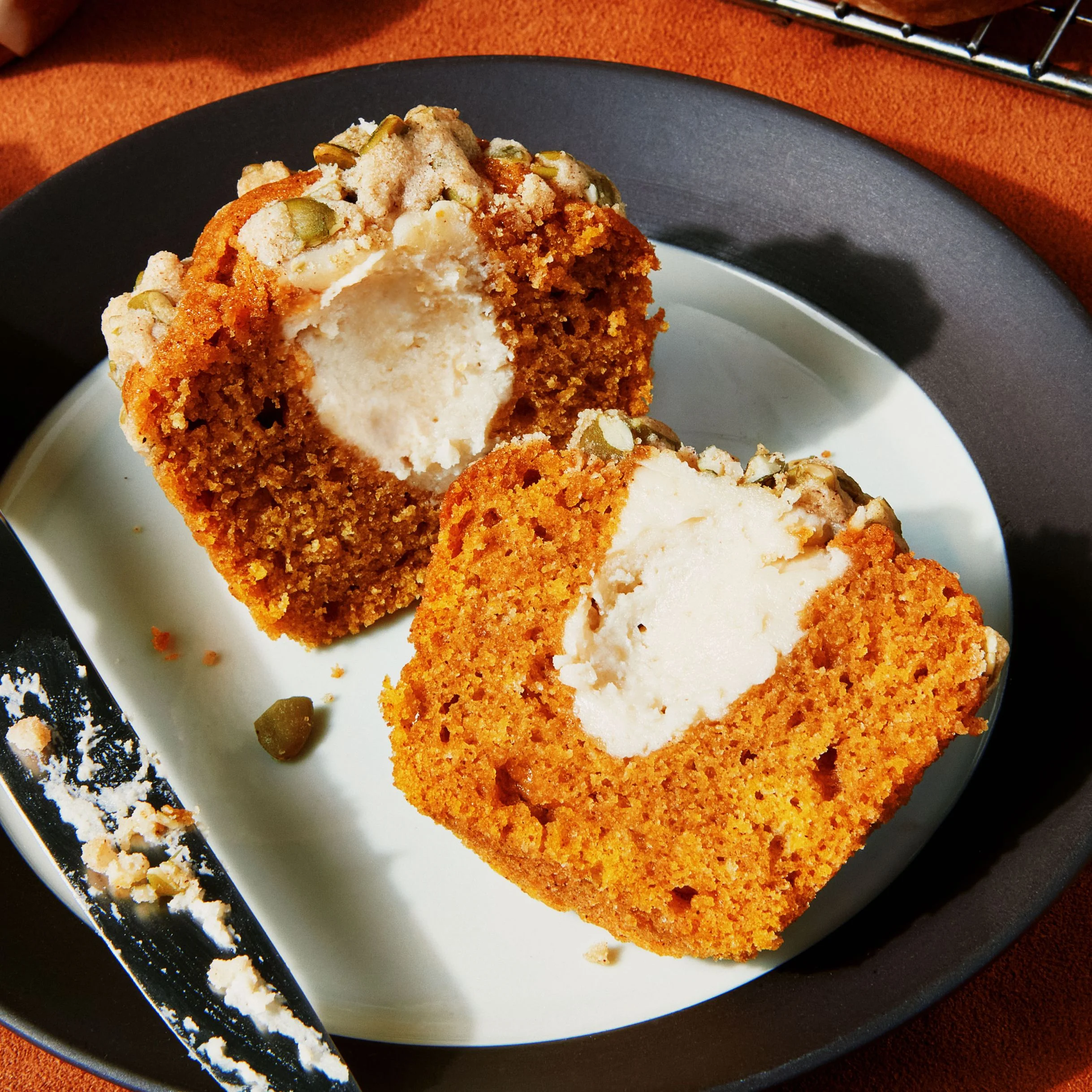 Pumpkin muffins filled with sweetened cream cheese and topped with pepita streusel.