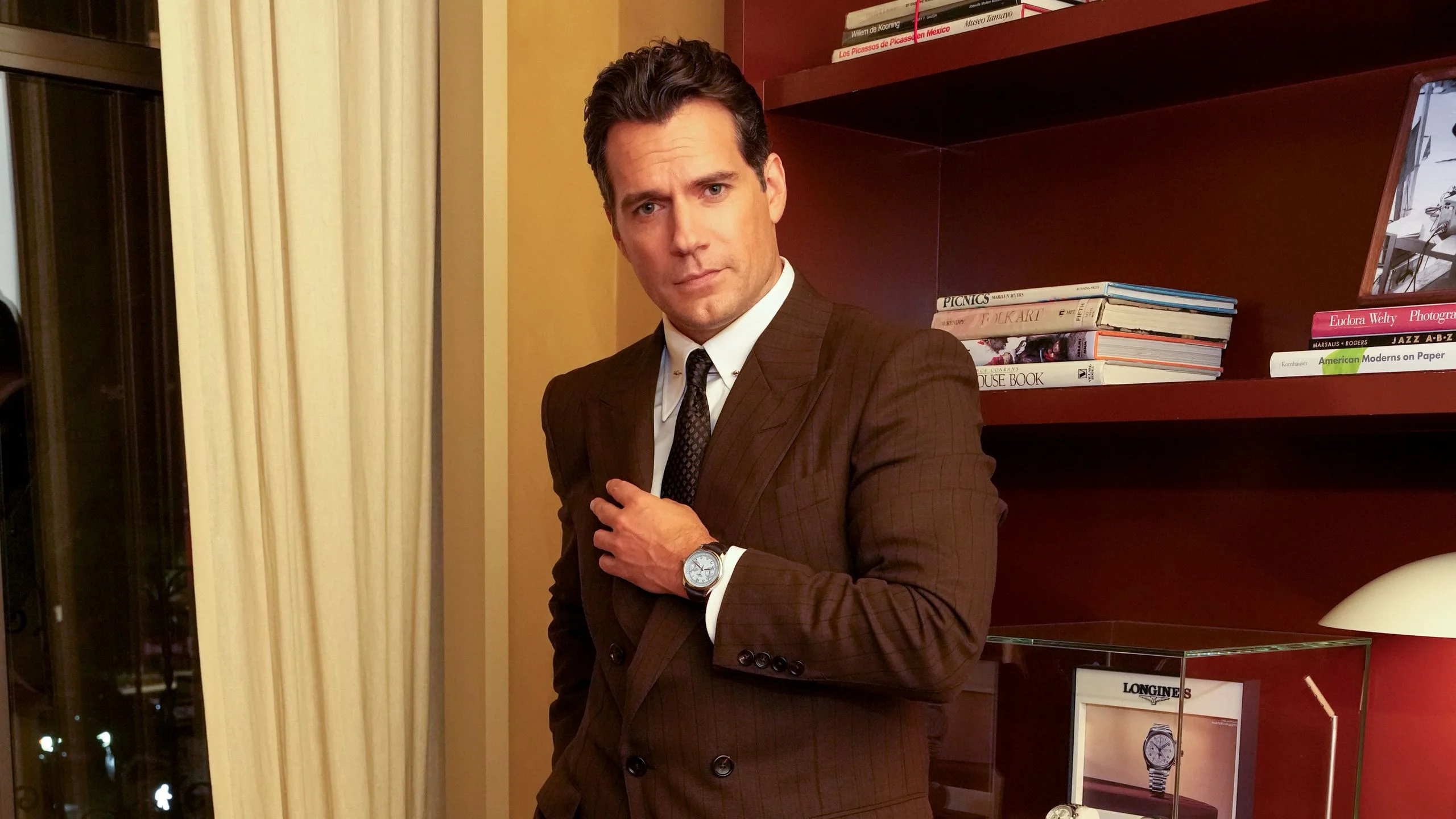 Image may contain Henry Cavill Blazer Clothing Coat Jacket Formal Wear Suit Person Standing Adult and Wristwatch
