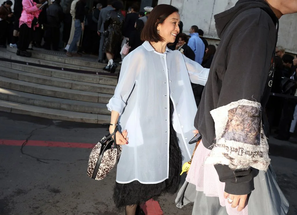Image may contain Yumi Masuda Adult Person Clothing Coat Accessories Bag Handbag Footwear Shoe Face Head and Hat