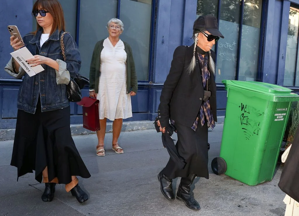 Image may contain Person Adult Clothing Coat Accessories Bag Handbag Footwear Sandal Hat Mailbox and Glasses