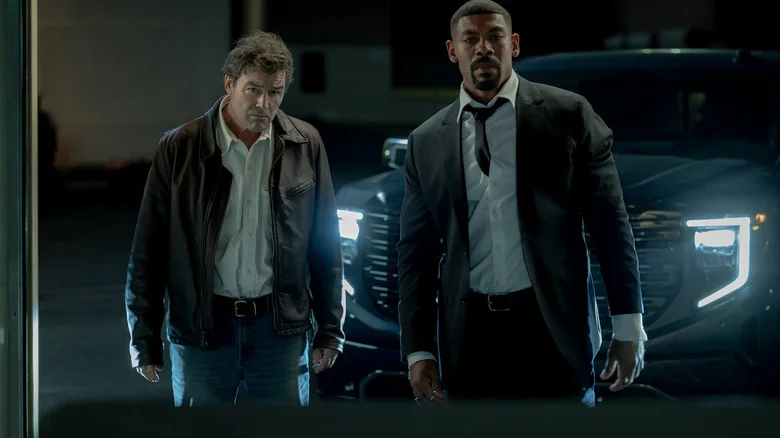 Kyle Chandler as Hal Jordan standing next to Aaron Pierre as John Stewart in front of a running SUV in Lanterns