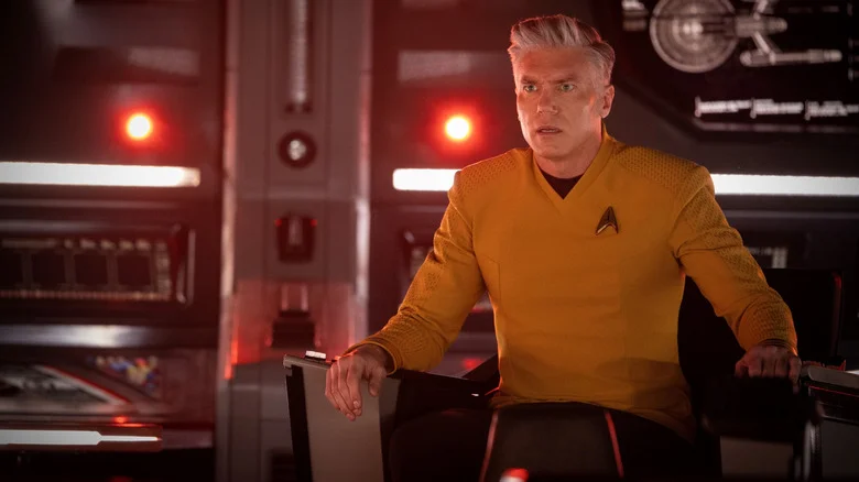 Anson Mount as Christopher Pike seated at the captain's chair on a starship with red emergency lights flashing behind him in Star Trek: Strange New Worlds