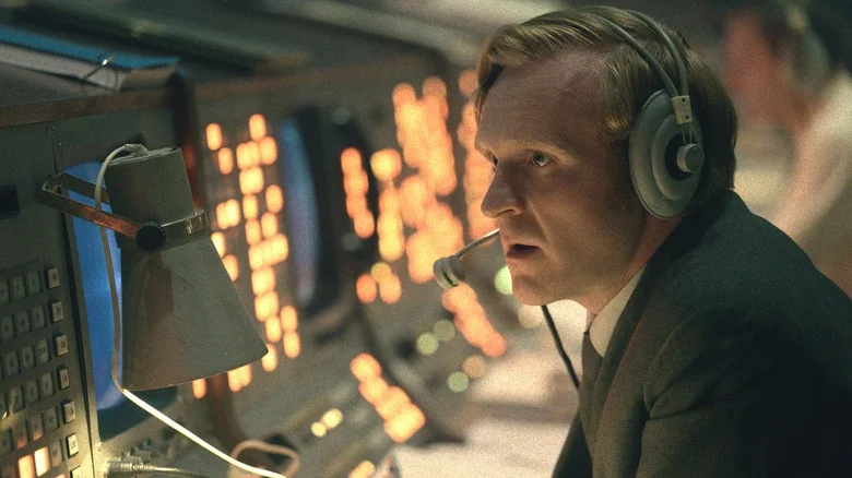 Josef Davies as Sergei Nikulov wearing a headset and sitting by a series of consoles in Star City